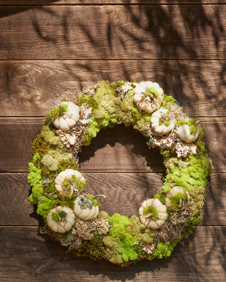 a wreath made from moss lichen and mini white pumpkins hung on a brown barn