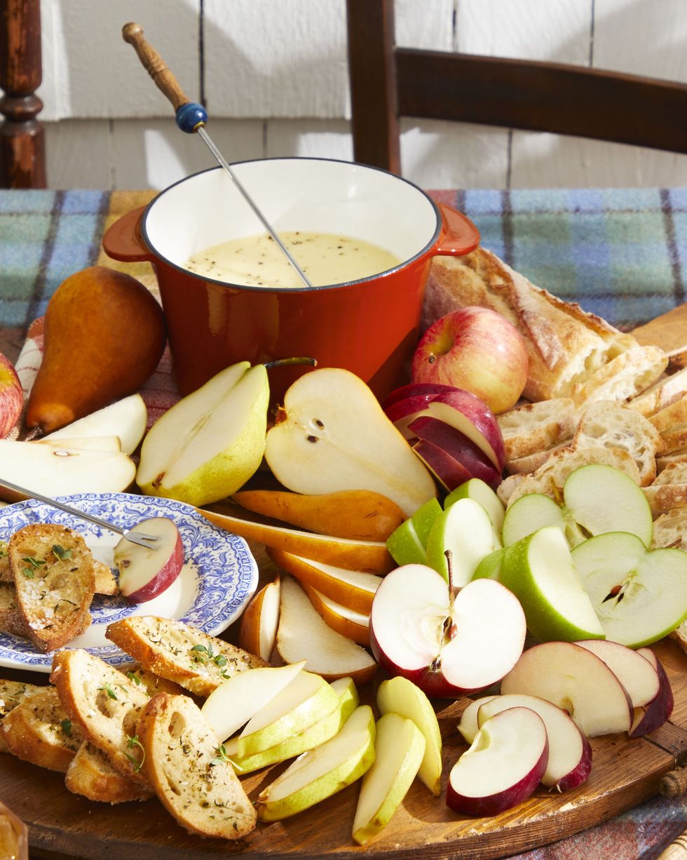 apple cider fondue on a plate with slices of fruit and bread, all on an outdoor table