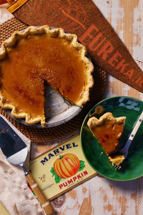 pumpkin pie in a metal pie tin with a slice removed and on a dark green plate next to it with a fork