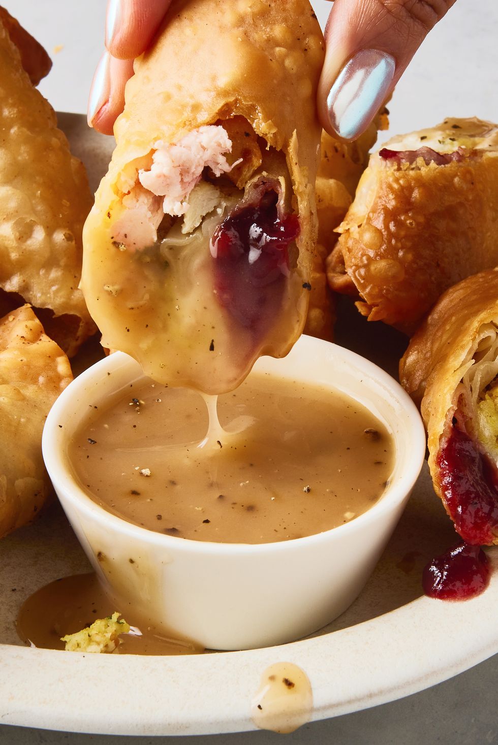 egg rolls stuffed with thanksgiving ingredients like cranberry sauce, stuffing, and mashed potatoes alongside a ramekin of gravy