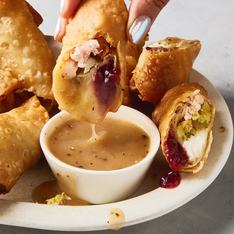 egg rolls stuffed with thanksgiving ingredients like cranberry sauce, stuffing, and mashed potatoes alongside a ramekin of gravy