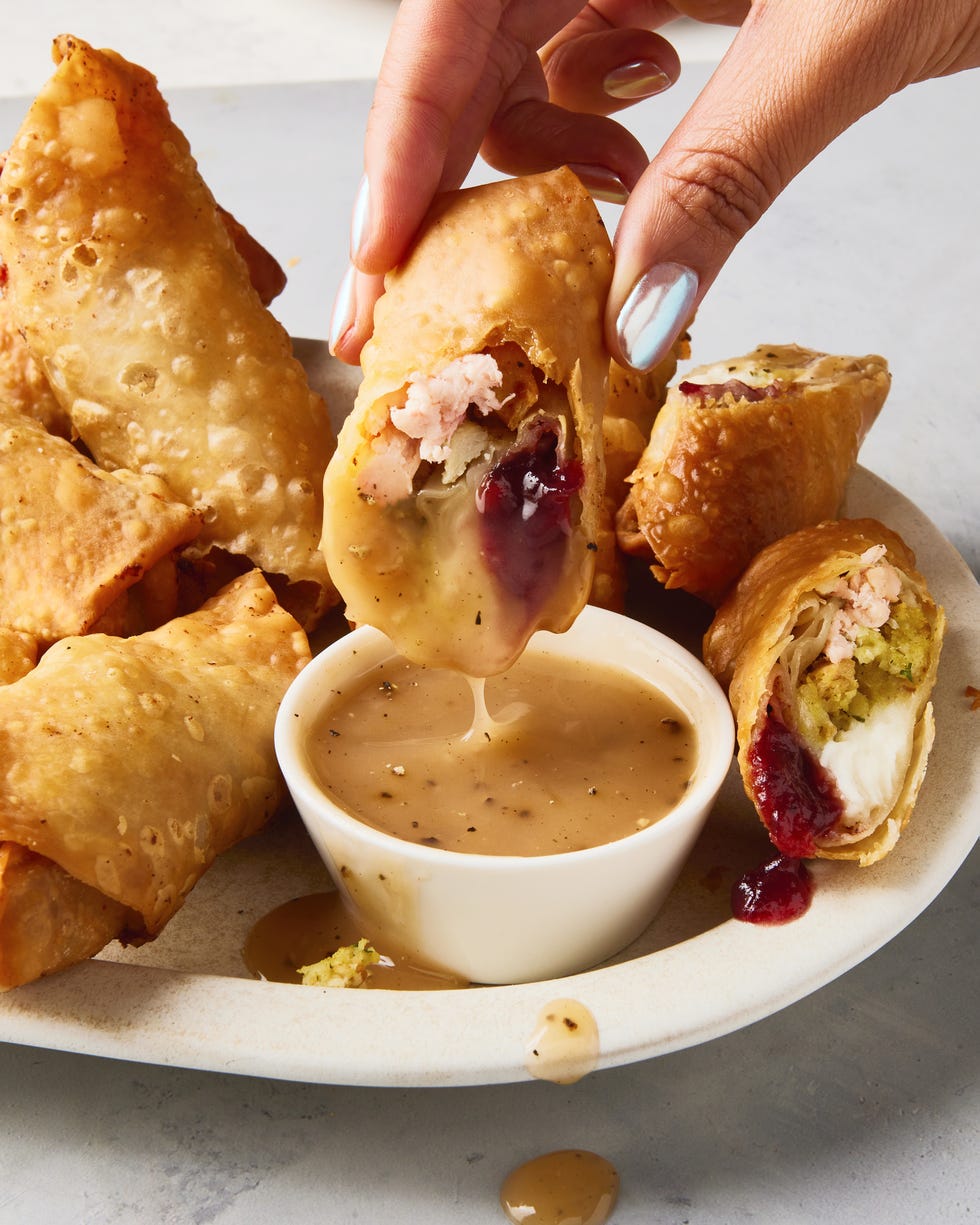 egg rolls stuffed with thanksgiving ingredients like cranberry sauce, stuffing, and mashed potatoes alongside a ramekin of gravy