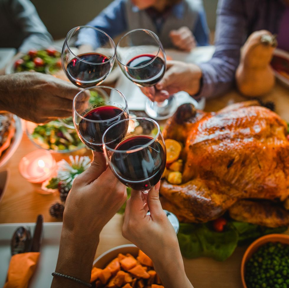group of unrecognizable people toasting with wine during thanksgiving dinner at dining table