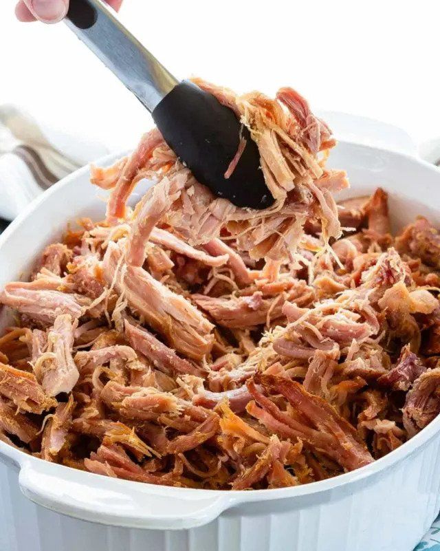 brown sugar baked ham shredded in white dish with tongs