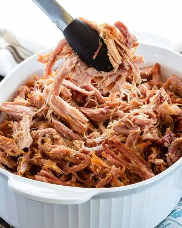 brown sugar baked ham shredded in white dish with tongs