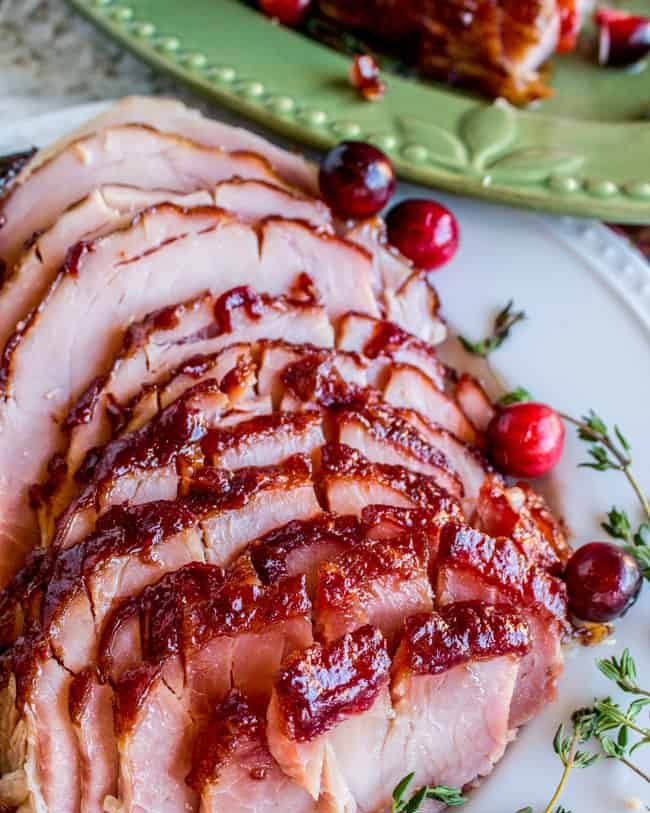 cranberry dijon glazed ham sliced on white platter with cranberries and rosemary