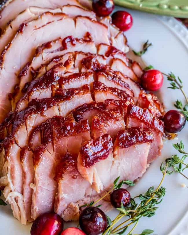 cranberry dijon glazed ham sliced on white platter with cranberries and rosemary
