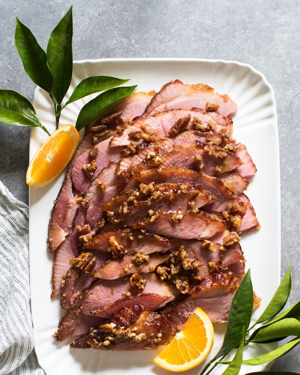 orange bourbon and pecan glazed ham sliced on white platter with leaves