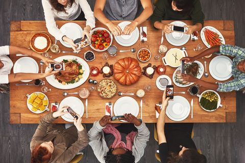 overhead view of friends gathered around thanksgiving table all taking food photos on their phones to post on instagram