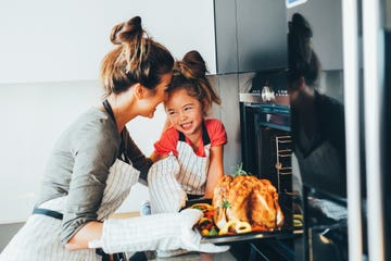 little girl watching her mother taking the turkey out of the oven