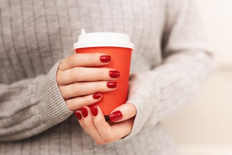 beautiful female hands with perfect red manicure holding a red cup of coffee
