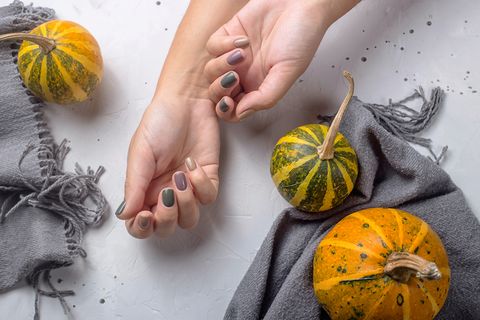 trend manicure in autumn colors on a gray table next to pumpkins and a gray scarf