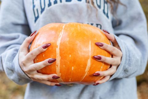 womens hands hold freshly picked large organic orange pumpkin outdoors, close up preparing for thanksgiving or halloween autumn seasonal healthy homemade food