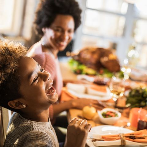 cheerful black girl laughing while having a meal with her parents in dining room
