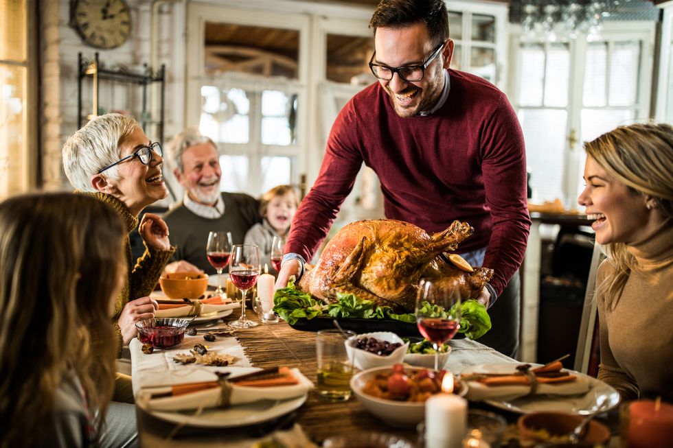 happy man serving roasted turkey to his family during thanksgiving dinner at dining table