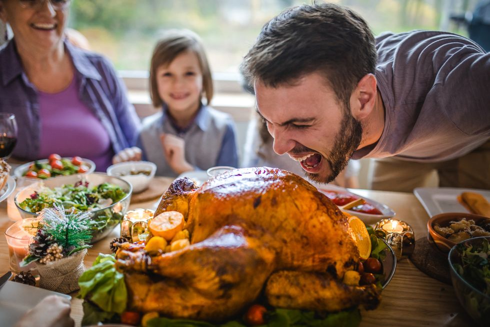 young man having fun while about to bite a stuffed turkey during thanksgiving dinner in dining room