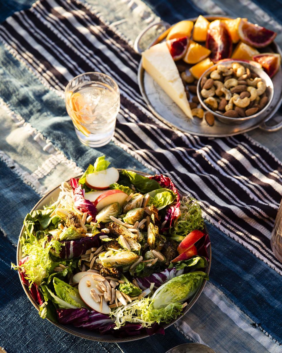 crispy brussels sprouts salad in a bowl on a tablecloth with cheese and fruit and nuts near by
