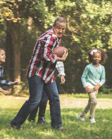 multi ethnic, multi generation family members playing a football game together in grandparents backyard on thanksgiving day  family in sports