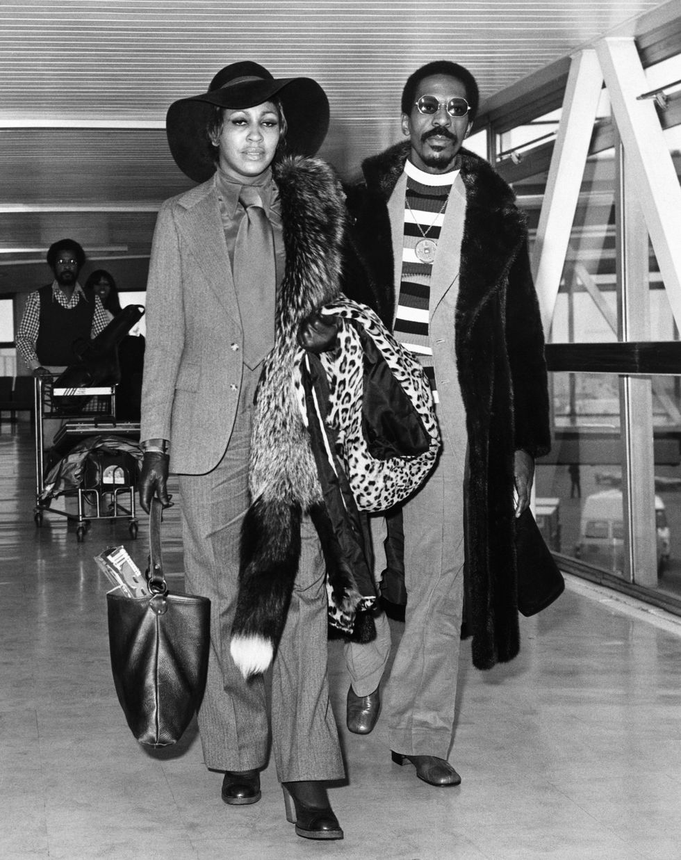 tina and ike turner walk inside a building carrying bags and coats