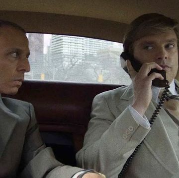a man talking on a cell phone next to a man in a car