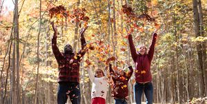 family with different skin tones standing in fall forest throwing up leaves