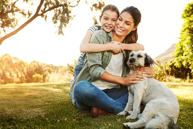 una niña abraza a su madre en un parque donde están con su mascota