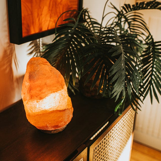 an orange himalayan salt lamp in a domestic environment beside a house plant it is on, giving a warm, soft glow