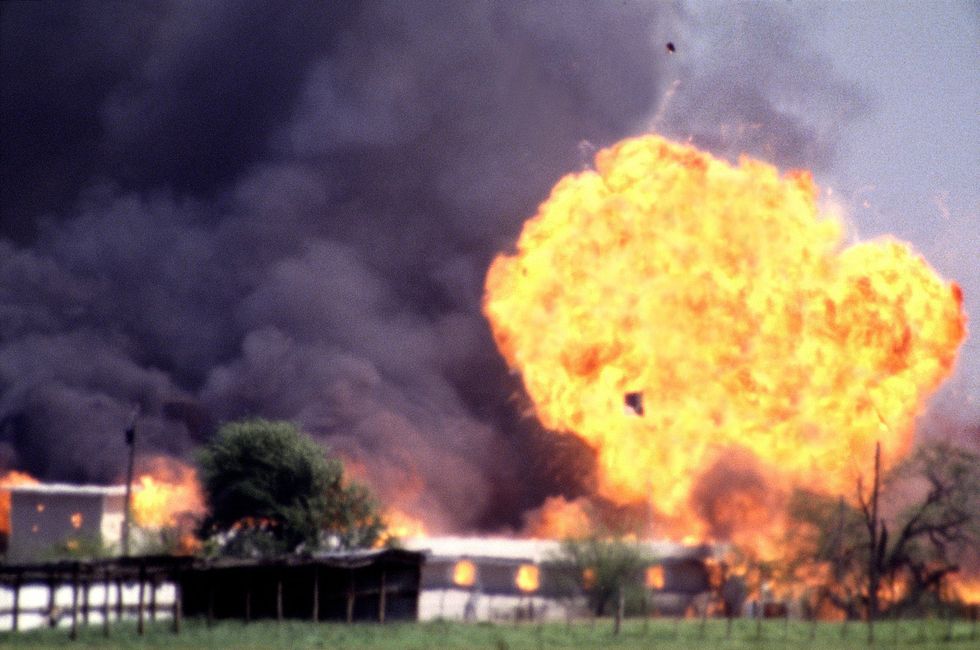 a large fireball erupts from a compound, sending black smoke into the air