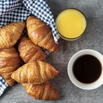 view from above of a cup of coffee and a glass of orange juice next to rich little croissants ready for breakfast on a gray stone table copy space