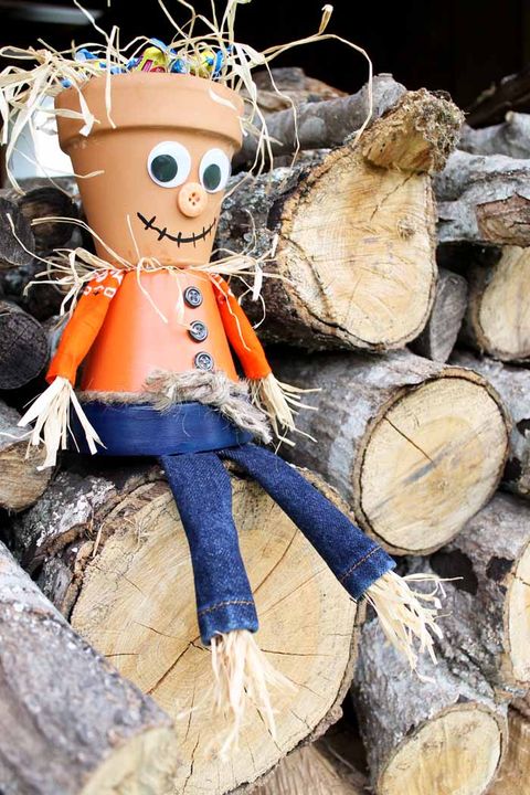 scarecrow made out of two clay pots, one for head, one for body, sitting on top of a wood pile