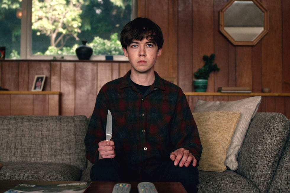 un chico con un cuchillo en la mano sentado en un sofá en la serie the end of the fucking world