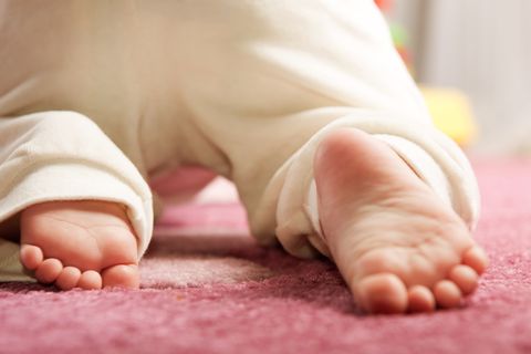 The feet of a baby crawling on a pink carpet