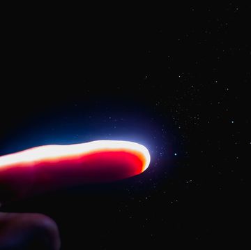 the finger is illuminated by a bright beam of light in the dark with flying dust particles