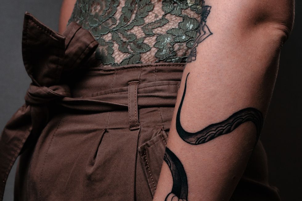 the forearm of a young woman she is tattooed a rose decorates her hand she wears a green lace top and brown pants