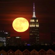 full moon rises behind the empire state building in new york city