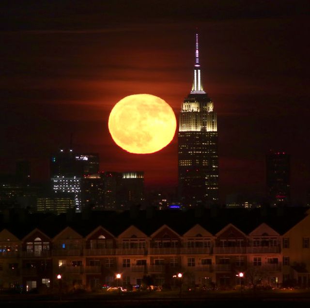 full moon rises behind the empire state building in new york city