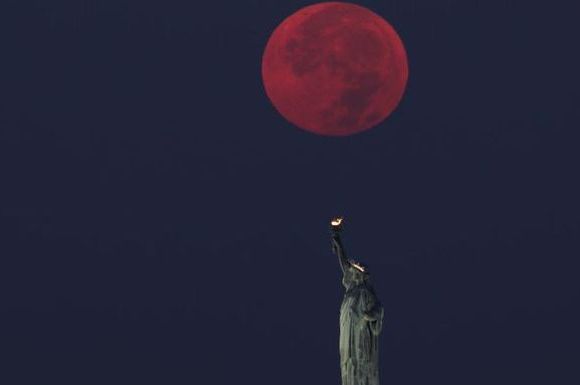 full moon sets behind the statue of liberty in new york city