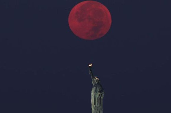 full moon sets behind the statue of liberty in new york city