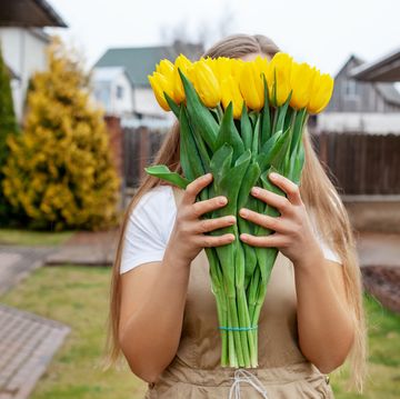 the girl hides her face behind a large bouquet of yellow tulips women's day, valentine's day