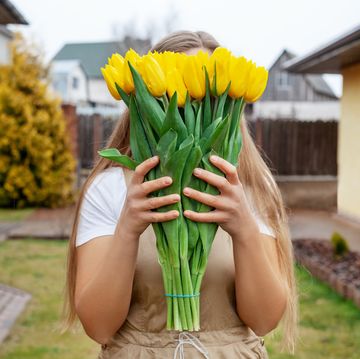 the girl hides her face behind a large bouquet of yellow tulips women's day, valentine's day