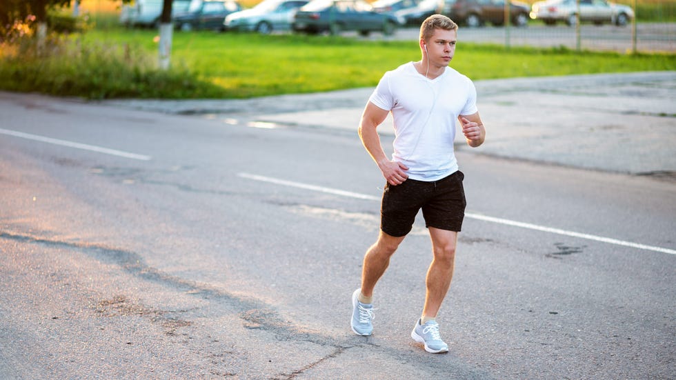 the guy runs through the city in shorts in the evening joint exercises jogging a man in the park listens to an audiobook, a confident look summer lifestyle, motivation is strong