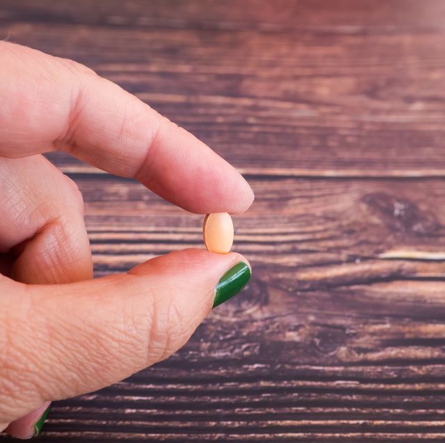 the hand of a person with one pill on her fingers