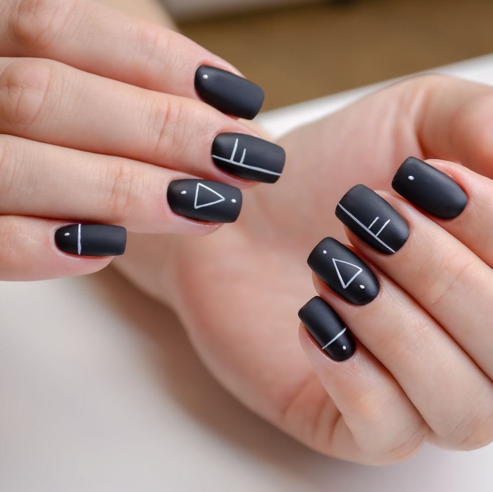 the hands of a young woman with a black matte gel polish and geometric design manicure ideas