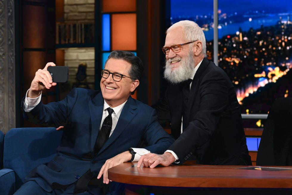 stephen colbert sitting down and holding his phone out for a selfie with david letterman