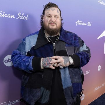 jelly roll crossing his hands while smiling for a photo in front of an american idol backdrop