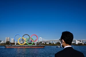 un hombre japonés con mascarilla observa la instalación de los aros olímpicos en la bahía de tokio el 1 de diciembre de 2021