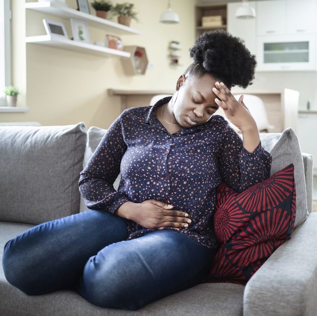 abdominal migraine woman holding her stomach and head while sitting on a gray couch