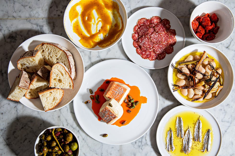 assorted dishes featuring bread olives meats and seafood on a marble surface