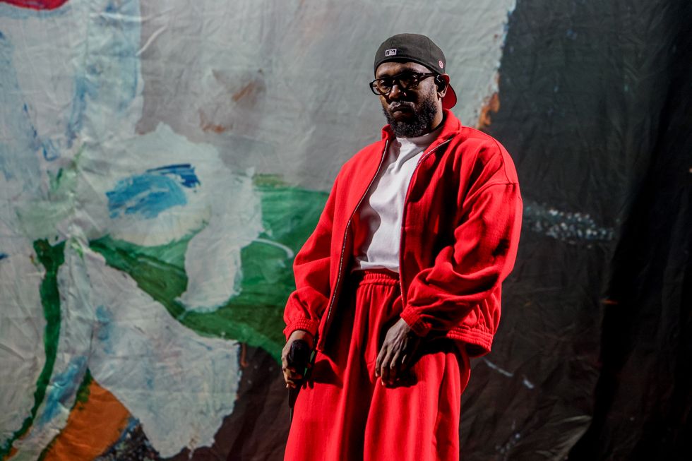 kendrick lamar stands in front of a multicolor wall and holds a wireless microphone