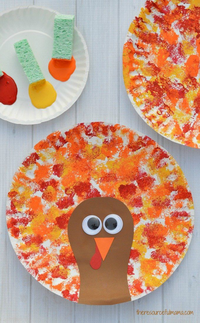 paper plate with turkey head with googly eyes, sponge painted "feathers" in orange, red and yellow, and another plate with green sponges dipped in red, orange and yellow paint